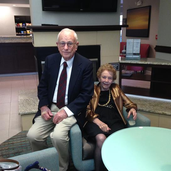 An elderly couple sits comfortably in a spacious lounge, sharing smiles and warmth.
