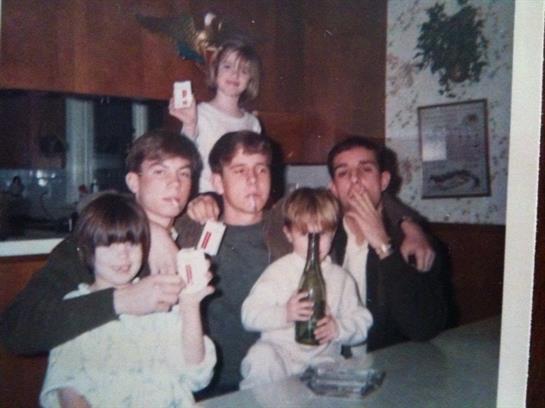Friends and family gather in a warm kitchen celebrating an occasion, holding drinks and showing joy.