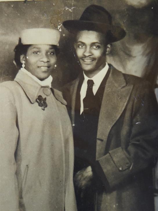 A vintage couple stands close, showcasing elegant outfits and joyful smiles in the studio.