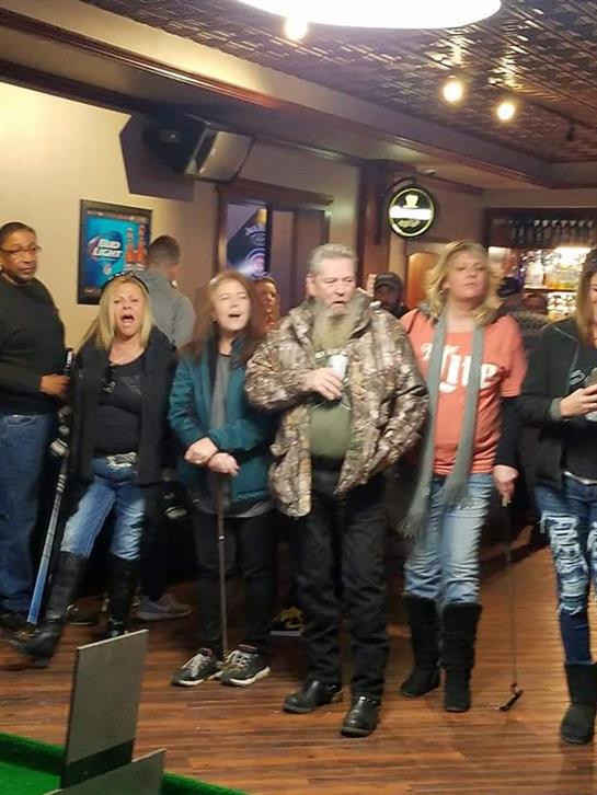 Friends gather in a bar, joyfully singing and enjoying their time together at night.