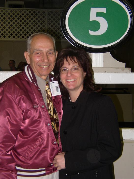 A joyful couple poses together at a racetrack, dressed stylishly and sharing a moment of happiness.