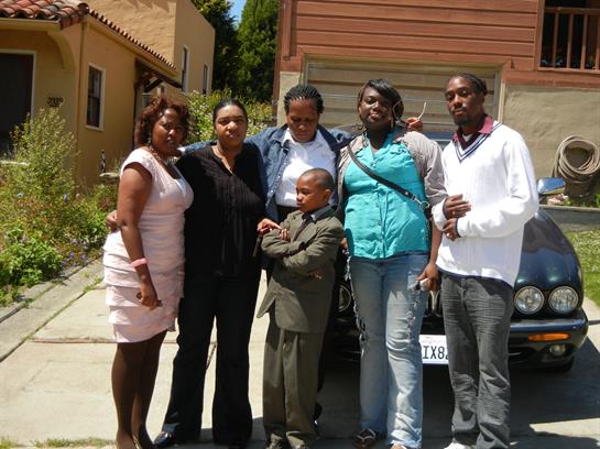 Six individuals gather together, smiling and dressed for a special occasion outside a home.