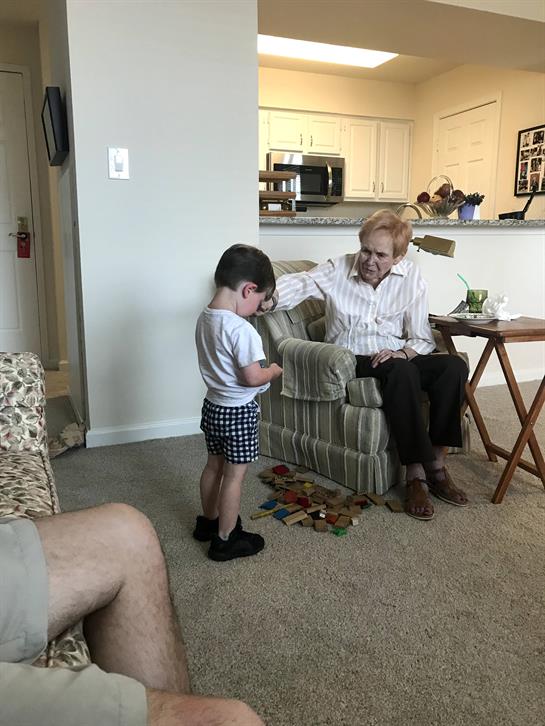 An elderly man sits in a chair while a young boy stands nearby, engaged in conversation.