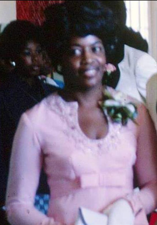 A woman in a pink dress is part of a formal gathering, smiling as she interacts with guests nearby.
