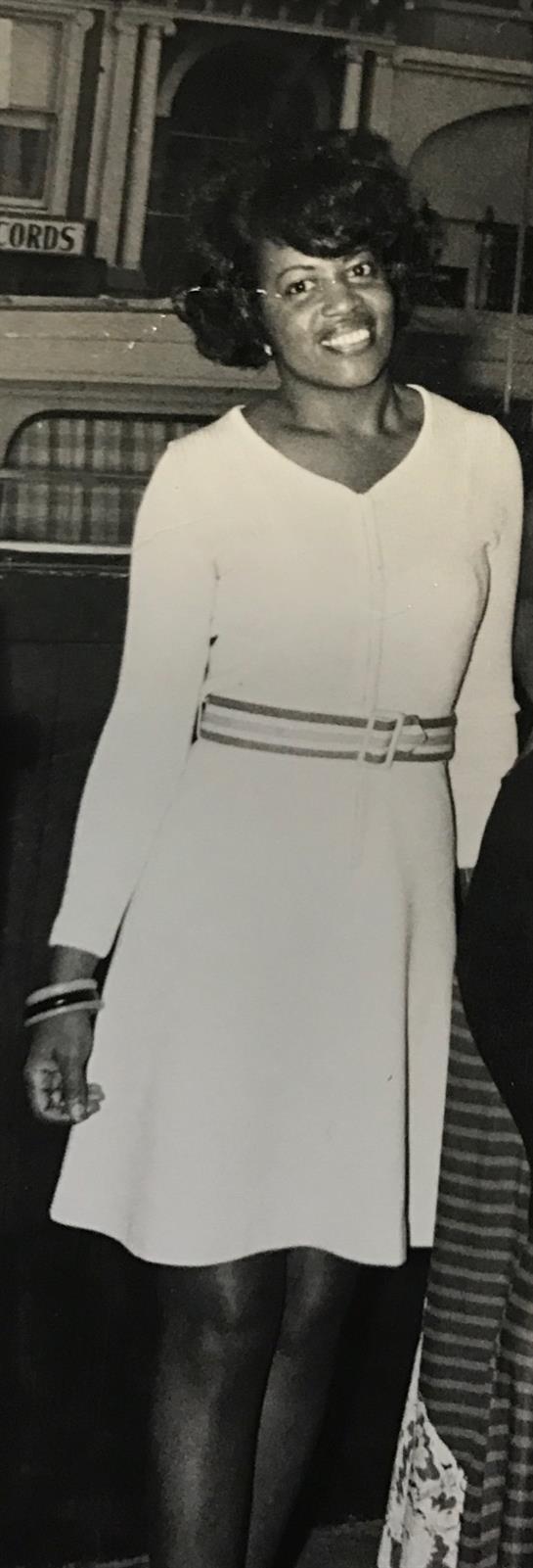 Woman poses in a stylish white dress with a belt, showcasing elegance at a social event.
