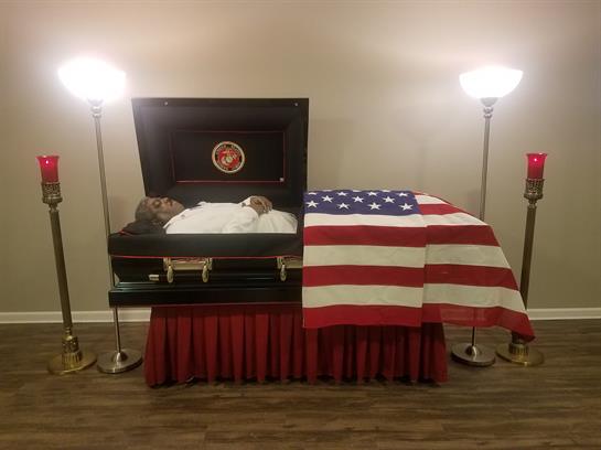 A casket under soft lighting and an American flag creates a reflective atmosphere.