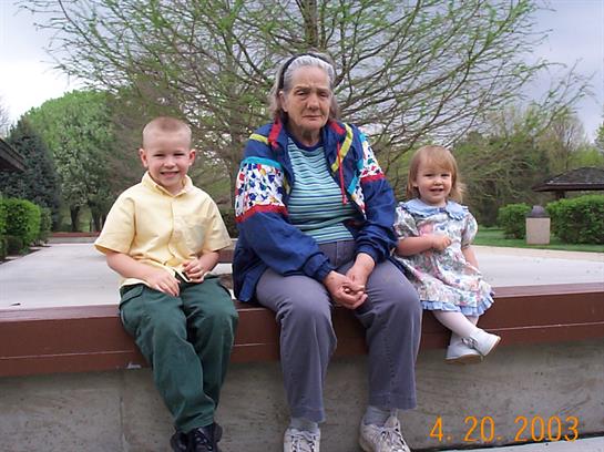 Two young children sit beside an elderly woman in a park, sharing smiles and laughter.