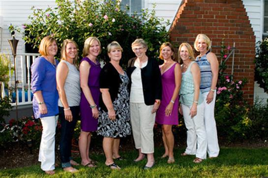 Women stand side by side in a garden, smiling and enjoying a summer gathering in the evening light.