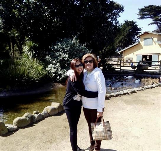 Women enjoy time together by a pond, smiling and embracing in a picturesque outdoor setting.