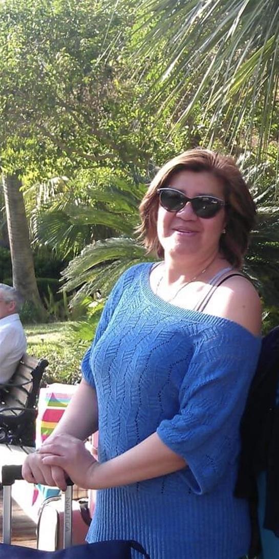 Woman wearing sunglasses and a blue sweater smiles while enjoying a sunny day outside.