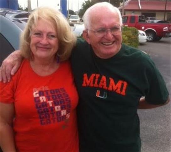 Couple poses joyfully in team shirts outside, showcasing their support for rival sports teams.