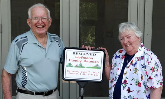 Smiling couple holds a reunion sign at a family gathering in a sunny location on a summer day.