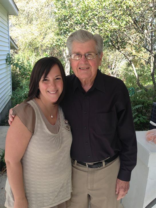 Two people stand closely together, smiling joyfully in a lush garden filled with greenery.