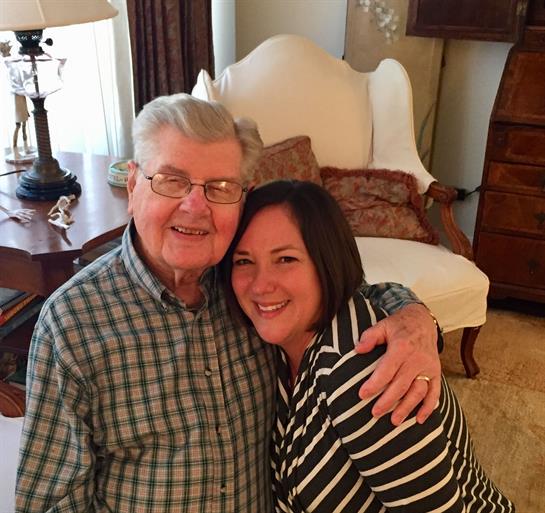 A younger woman and an elderly man share a warm embrace, smiling happily together.