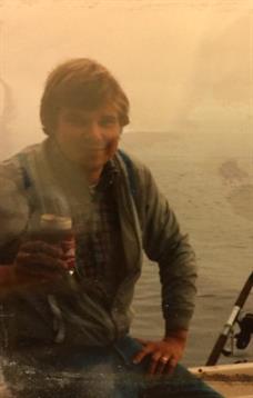 Person is smiling and holding a drink while relaxing by the water during sunset.