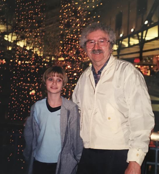 A happy boy stands with an older man amid colorful holiday lights.