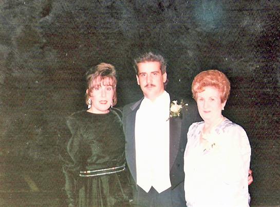 Three people in formal wear enjoy a moment at a dimly lit celebration.