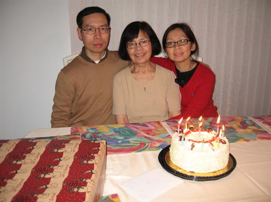 Family members joyfully gather around a decorated table with a birthday cake during a celebration.