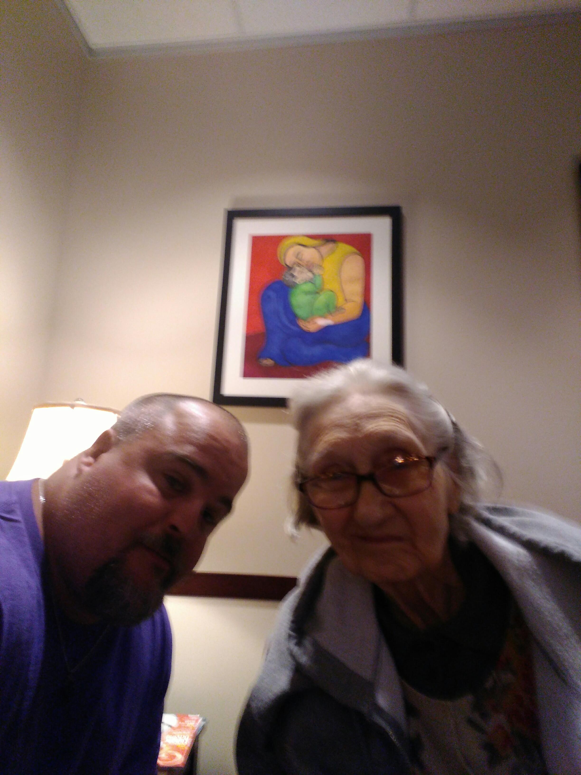 Man and elderly woman smile together in a warmly lit room featuring vibrant artwork on the wall.