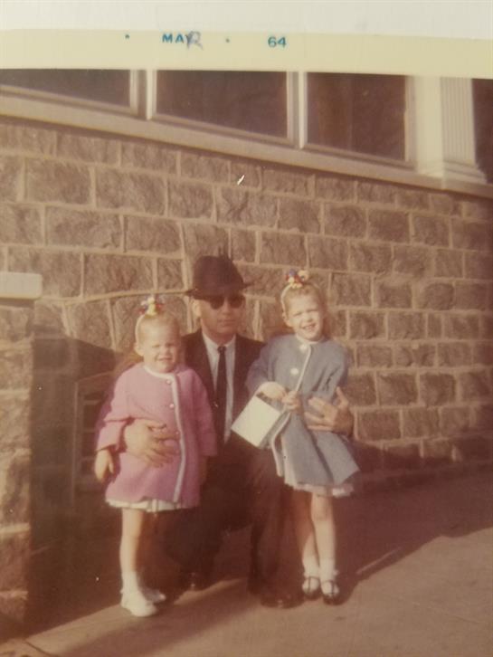 Girls dressed in coats pose with a man in front of a stone wall during daylight.