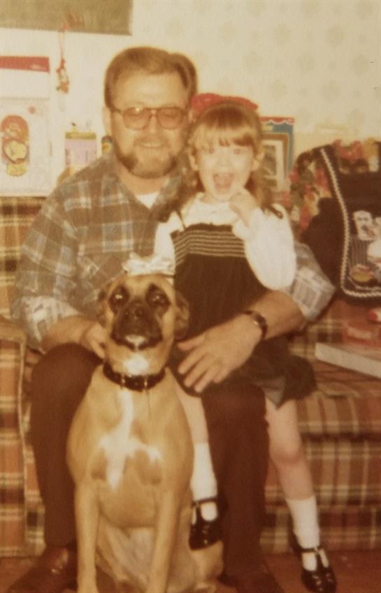 A young girl and her grandfather share a joyful moment with a dog in their home from the 1980s.