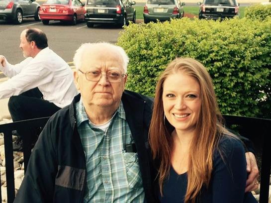 A woman poses with her grandfather, smiling together outdoors in a lively environment.