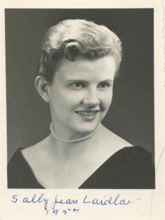 Woman wearing a black gown with a pearl necklace smiles gracefully in a portrait taken indoors.
