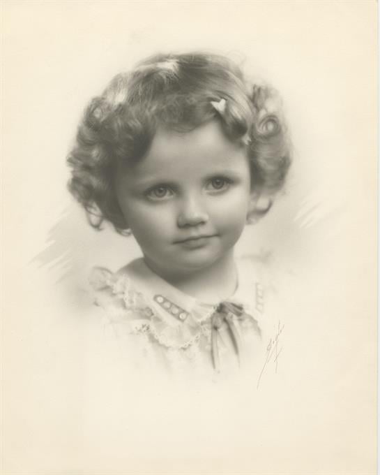 A young girl with curly hair and a soft expression poses elegantly in a vintage portrait.