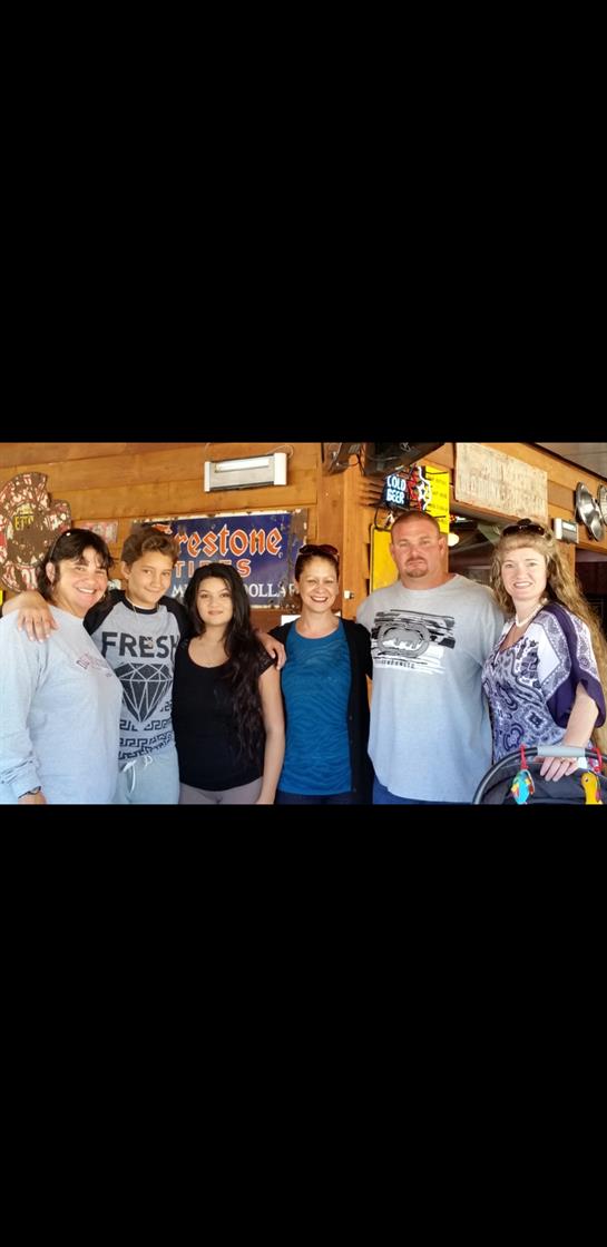 A joyful gathering of six people posing together in a cozy, rustic bar environment.