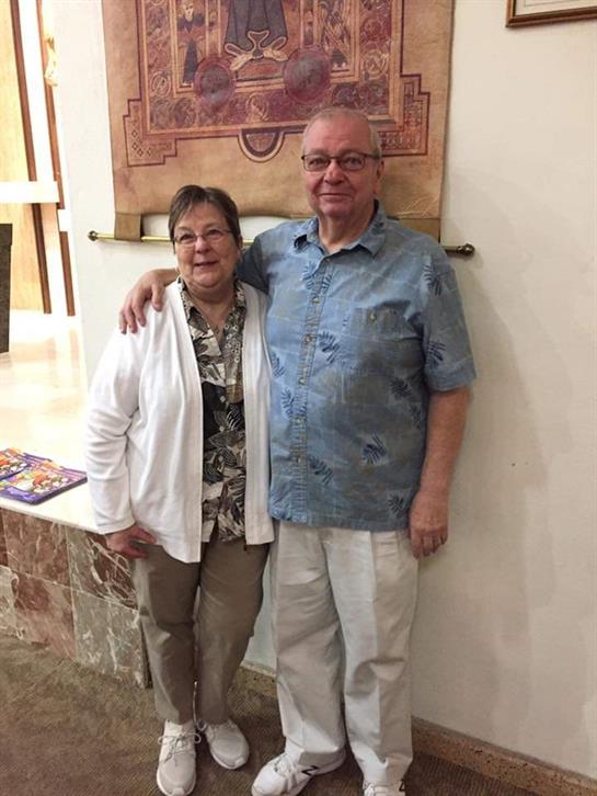 Couple stands close together, smiling warmly in a cozy indoor environment, enjoying a social moment.