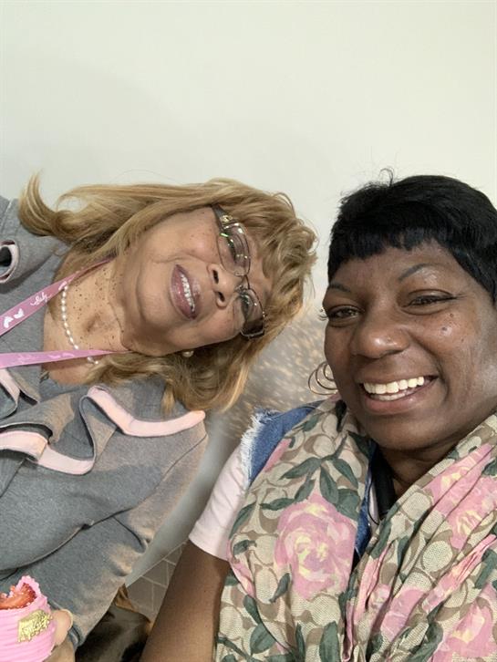 Two women pose together, smiling and enjoying a social gathering at a friendly event.