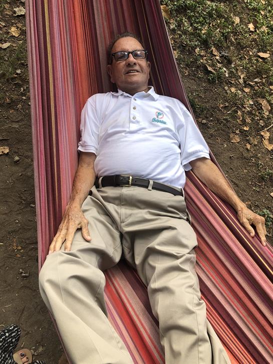 A man is lounging comfortably in a colorful hammock, enjoying the tranquility of nature.