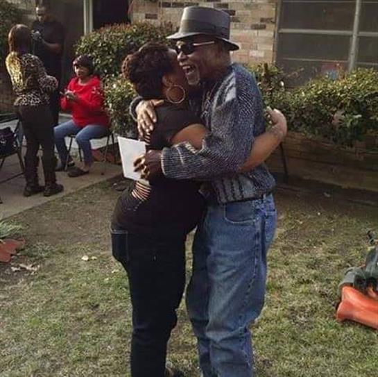 Friends embrace warmly in a lively community gathering while others socialize in the background.