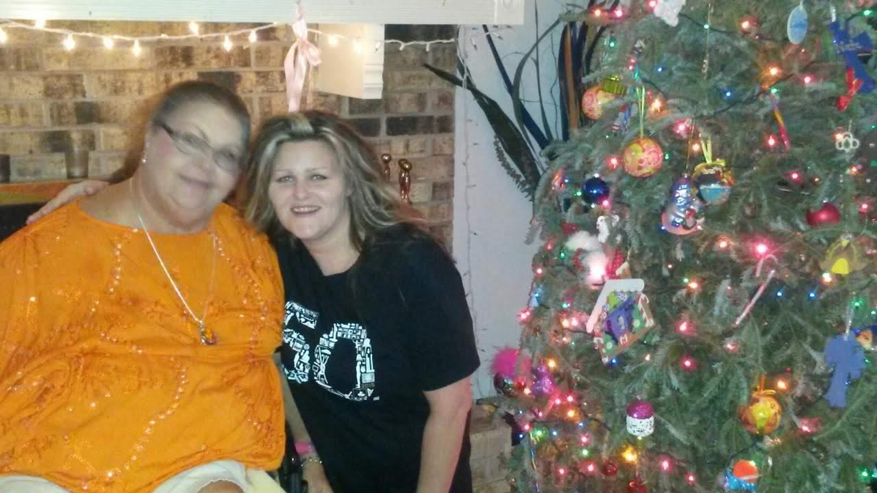 Two women joyfully pose together, celebrating a special birthday next to a decorated Christmas tree.