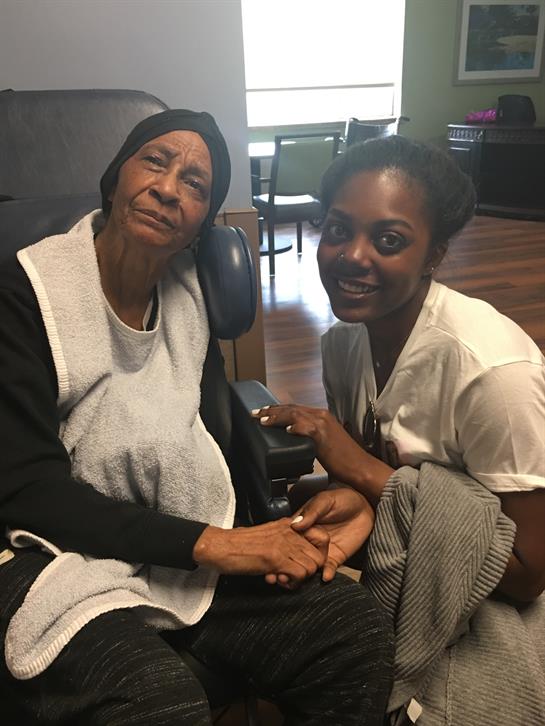 Two women sit together in a care facility, sharing a heartwarming moment during a visit.