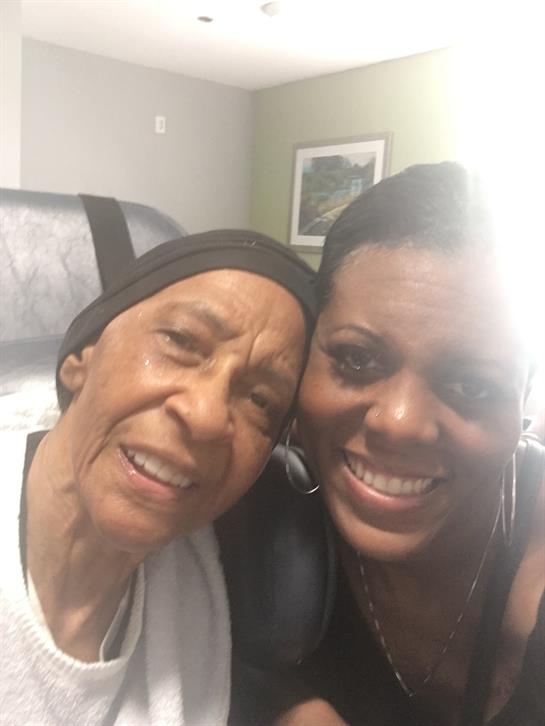 Two women embrace and smile for a joyful close-up portrait in a warm indoor environment.