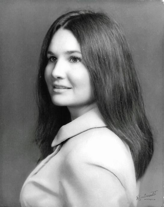 A young woman stands confidently, showing her long hair and elegant attire while posing gracefully.