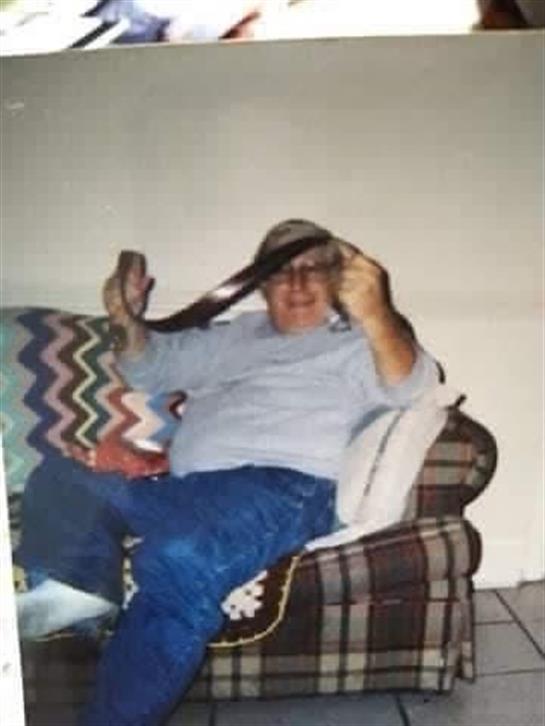 A man with a joyful demeanor holds a hat and sits comfortably on a couch.