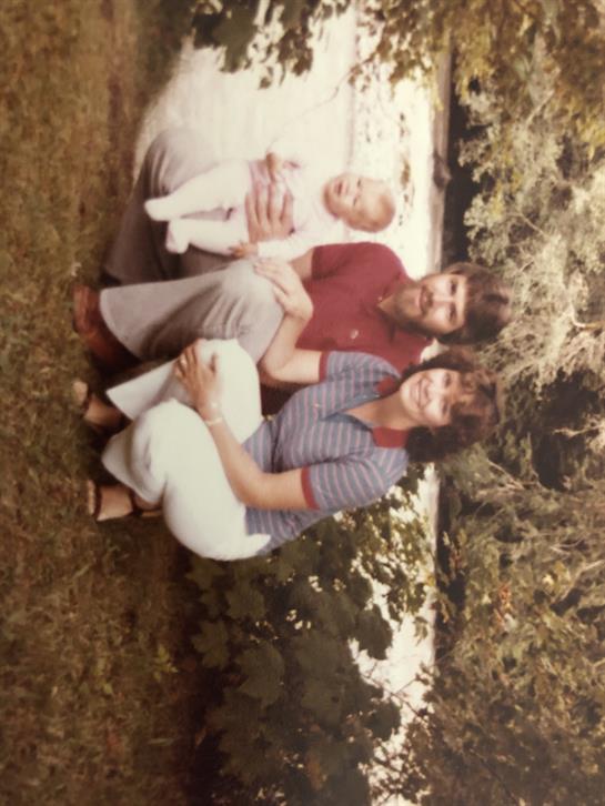 A joyful family poses by a river with a baby, capturing a moment of togetherness outdoors.