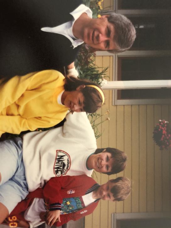 A group of four people smiles warmly while sitting together in a backyard on a sunny day.