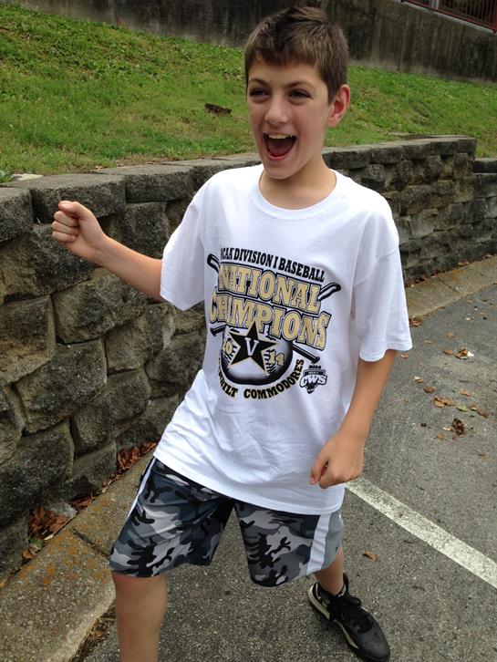 Young boy shows joy and excitement while playing outside near a stone wall on a sunny day.