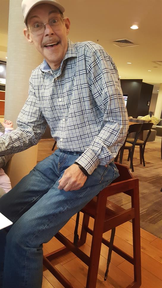 A man wearing a plaid shirt is talking with a friend in a casual setting surrounded by modern decor.