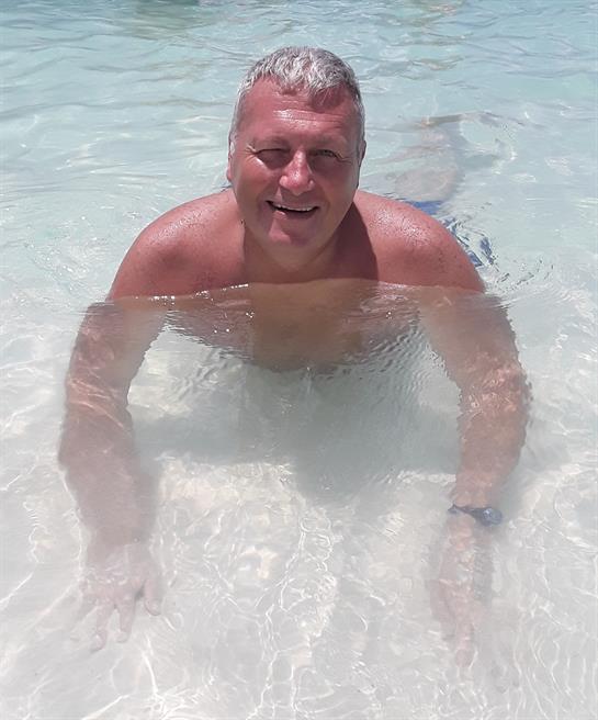 Relaxation takes place as a man smiles while wading in crystal-clear water on a sunny day.
