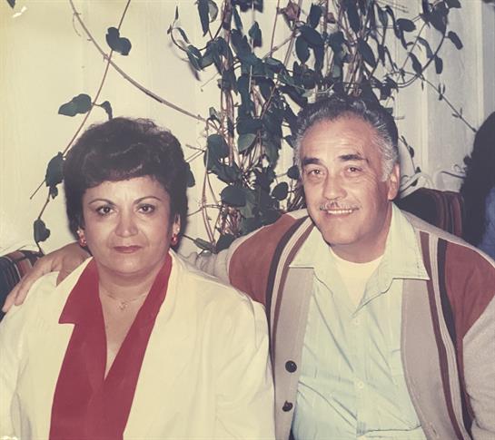 Couple smiles for the camera in a warm, inviting indoor space with plants around them.