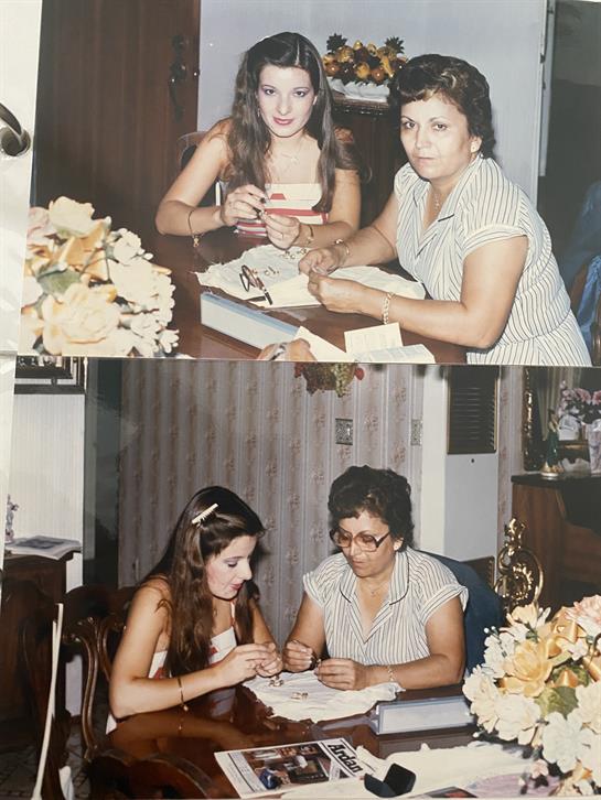 Two women sit at a table, focused on crafting together surrounded by flowers and family decorations.