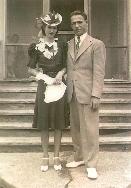A couple poses together wearing formal attire on wooden steps outside a building in the 1940s.