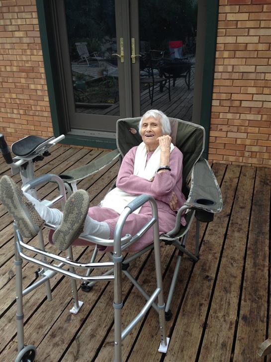 An elderly woman enjoys leisure time on a reclining chair, taking in the fresh air outside.