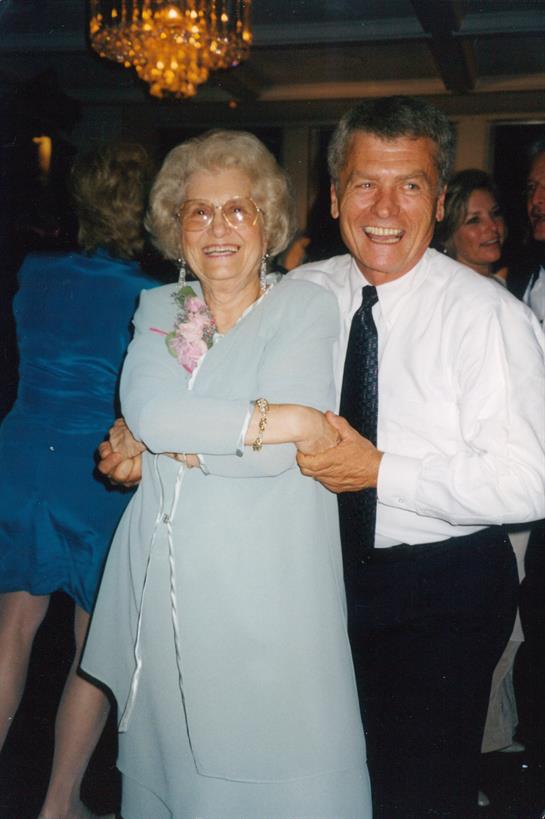 An elderly man and woman share a joyful dance at a vibrant gathering filled with smiles.