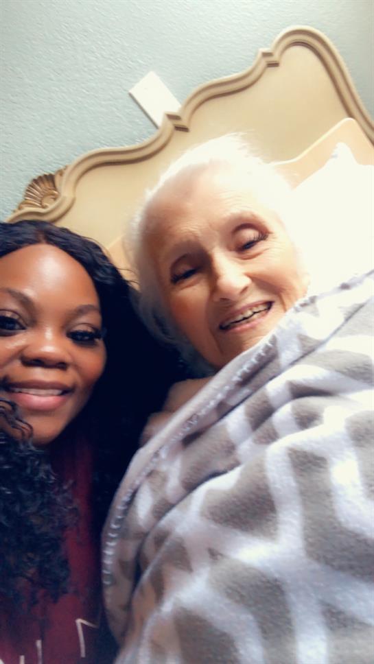 Caregiver and elderly woman share a joyful moment together, wrapped in a warm blanket with smiles.