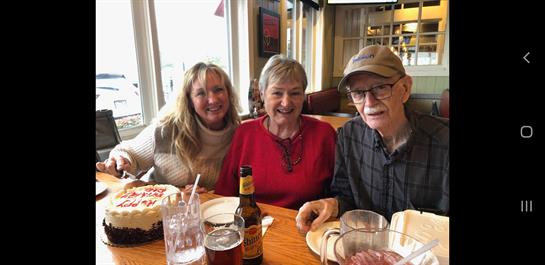 Three people share smiles and laughter while enjoying cake and drinks at a festive meal.